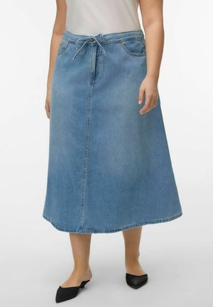 Frau trägt einen hellblauen Denim-Midirock mit vorderen Nähten, Gürtelschlaufen und Kordelzug, kombiniert mit schwarzen spitzen Schuhen.