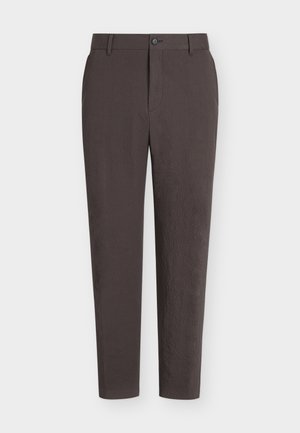 Sötétbarna, vékony szabású nadrág övbújtatókkal, elöl gombos és cipzáras rögzítéssel, egyszerű fehér háttéren bemutatva.