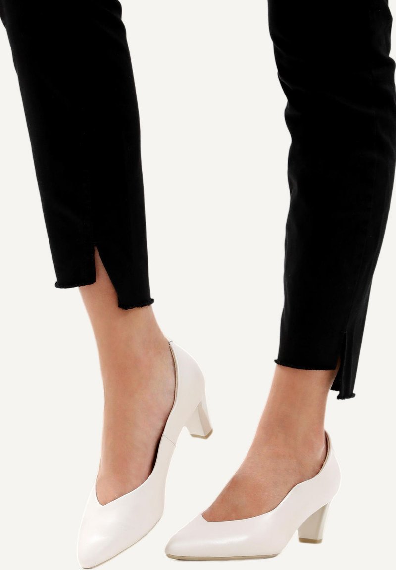 Décolleté in vernice bianca con tacco a blocco e punta affusolata, abbinati a pantaloni neri cropped con orlo grezzo e dettaglio di spacco laterale.