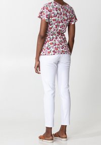 Blommig topp med korta ärmar i vitt, prydd med rosa och röda blommor; kombinerad med vita figursydda byxor och bruna platåsandaler.