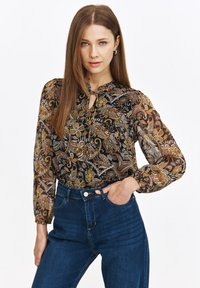 Luźna czarna bluzka z misternym wzorem paisley w odcieniach złota, brązu i zieleni. Posiada dekolt w kształcie klucza i długie rękawy.