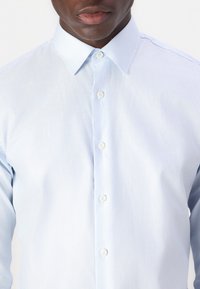 Light blue button-up shirt with a soft texture, featuring a classic collar and white buttons down the front. No visible patterns.