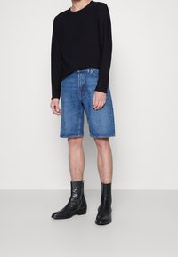 Schwarzes Langarmshirt, hellblaue Denimhorts und schwarze Lederstiefeletten. Das Outfit hat einen lässigen Stil und eine entspannte Passform.