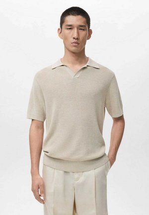 Beige Polohemd mit kurzen Ärmeln, V-Ausschnitt und kontrastierendem weißen Kragen; gerippte Struktur und lockere Passform, kombiniert mit hellen Hosen.