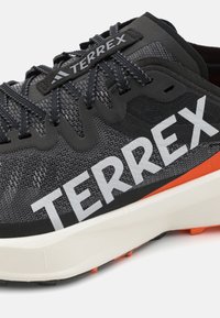 Black and gray athletic shoe featuring a breathable mesh upper, prominent white "TERREX" branding, and an orange accent on the sole.