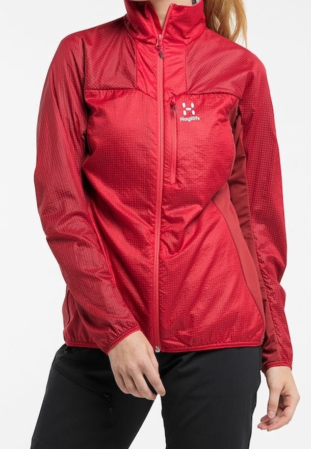 Femme portant une veste légère rouge avec fermeture éclair sur le devant et poche poitrine, associée à un pantalon noir.