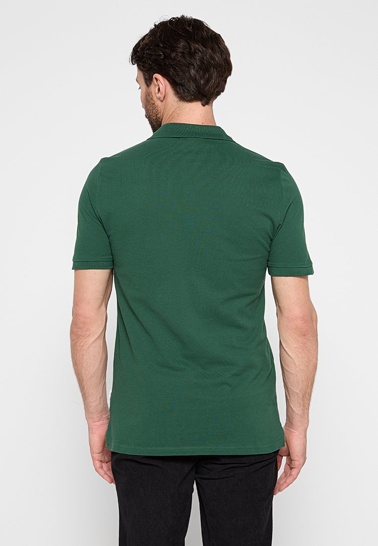 Polo shirt vert foncé à manches courtes, avec col côtelé et fentes latérales. Fabriqué en coton, il présente une texture lisse et un design épuré.