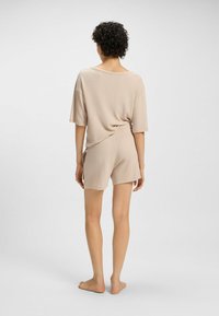 Beige loungewear set bestaande uit een losvallende, kortmouwige top en bijpassende shorts, gemaakt van een zachte, textuurrijke stof, met een open rugontwerp.