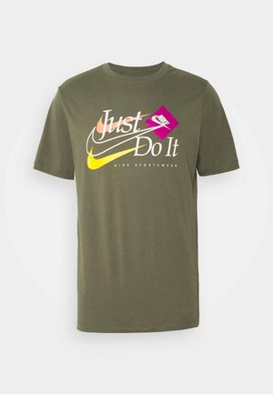 Oliwkowa koszulka Nike z wielokolorowym napisem „Just Do It”, dwoma zachodzącymi na siebie logo Swoosh oraz napisem „Nike Sportswear” poniżej wzoru.