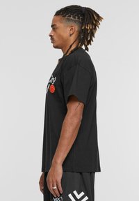 Sort bomulds t-shirt med korte ærmer, prydet med hvid tekst og et rødt basketballgrafik på forsiden. Casual pasform.