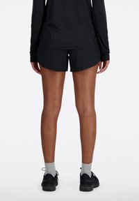 Pantalones cortos deportivos negros de material ligero, con un ajuste relajado y cintura elástica, combinados con zapatillas negras y calcetines grises.