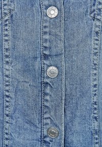 Jeansjacka i ljusblå nyans, med kontrasterande sömmar och fem silverfärgade tryckknappar framtill. Har en slät textur.