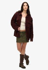 Burgunderfarvet corduroy skjortejakke med knaplukning, cremefarvet cropped top, olivengrøn cargo-nederdel og brune knæhøje støvler med hardware-detaljer.