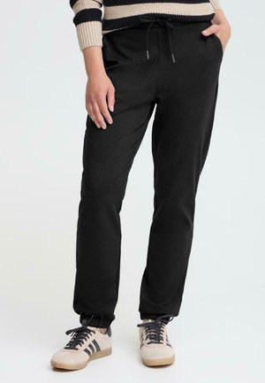 Sorte joggebukser med elastisk midjebånd, justerbar snøring og sidelommer. Kombinert med lyse sneakers.