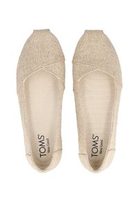 Ζευγάρι μπεζ υφασμάτινων παπουτσιών τύπου slip-on με κλειστή μύτη, επάνω μέρος με σταυροβελονιά και εσωτερικές σόλες με το λογότυπο "TOMS Wear Good".