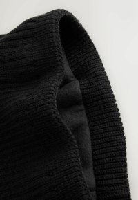 Sort ribbet strikstof med en glat fleece-indvendig. Foldet kantdetalje afslører kontrasterende teksturer og et blødt, varmt udseende.