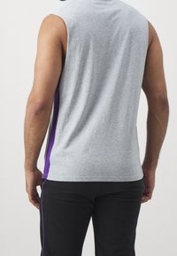 Szara bezrękawnik sportowy o gładkiej fakturze z purpurowymi bocznymi panelami, w połączeniu z czarnymi spodniami sportowymi z purpurowymi paskami.
