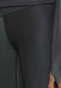Leggings sportivi neri con una texture liscia e elasticizzata e cuciture piatte, caratterizzati da un design aderente e accenti minimi.