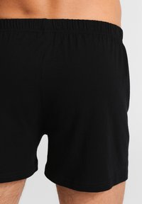 Boxer shorts de algodón negro con una cinturilla elástica, que presentan una textura suave y un diseño simple y clásico. Sin patrones ni acentos visibles.