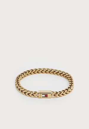 Bracelet en chaîne dorée comportant des maillons entrelacés, une finition lisse, et un fermoir avec un petit accent rouge et blanc.