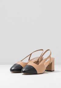 Beige leather slingback shoes with a black pointed toe cap and a block heel. Smooth texture with a wide, comfortable strap design.