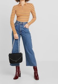 Polo a maniche lunghe a righe arancione e marrone, jeans blu a vita alta, borsa nera con catena argentata e stivaletti alla caviglia bordeaux lucidi.