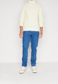 Pletený rolák v krémové barvě s žebrovanou texturou. Kombinován s modrými džínami a krémovými teniskami s gumovou podrážkou.