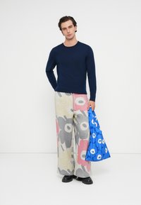 Námornícky sveter s dlhým rukávom, vzorované široké nohavice v sivej, červenej a béžovej farbe a jasne modrá taška s kvetinovým vzorom a rukoväťami.