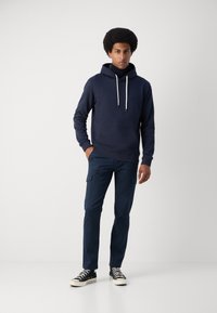 Sudadera con capucha navy con cordones, bolsillo frontal, combinada con pantalones cargo navy. El modelo lleva zapatillas negras de caña alta.