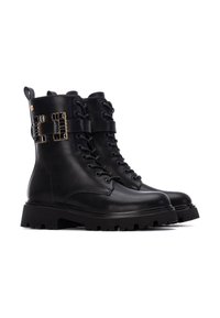 Botas de combate de piel negra con cordones en la parte delantera, cuello acolchado, acento distintivo de hardware dorado y suela de goma gruesa con tacos.