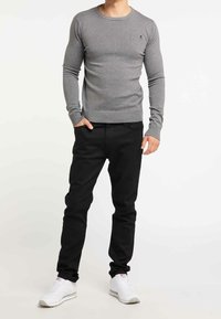 Pull en maille gris avec un col rond, des poignets et un ourlet côtelés ; porté avec un pantalon noir et des baskets blanches. Design simple et ajusté.