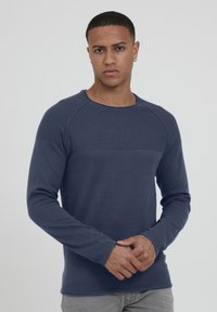 Cămașă lungă de culoare bleumarin, cu un corp texturat, guler rotund cu bordură și un panou contrastant pe piept. Material neted, design ajustat.