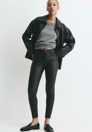 Zwarte faux leren jas, grijze sweatshirt en zwarte high-waisted skinny jeans. Accessoires zijn onder andere creolen en zwarte loafers.