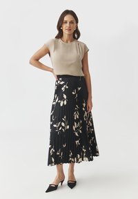 Blusa beige a maniche corte abbinata a una gonna plissettata nera con un motivo floreale. L'outfit è completato da décolleté neri a punta.