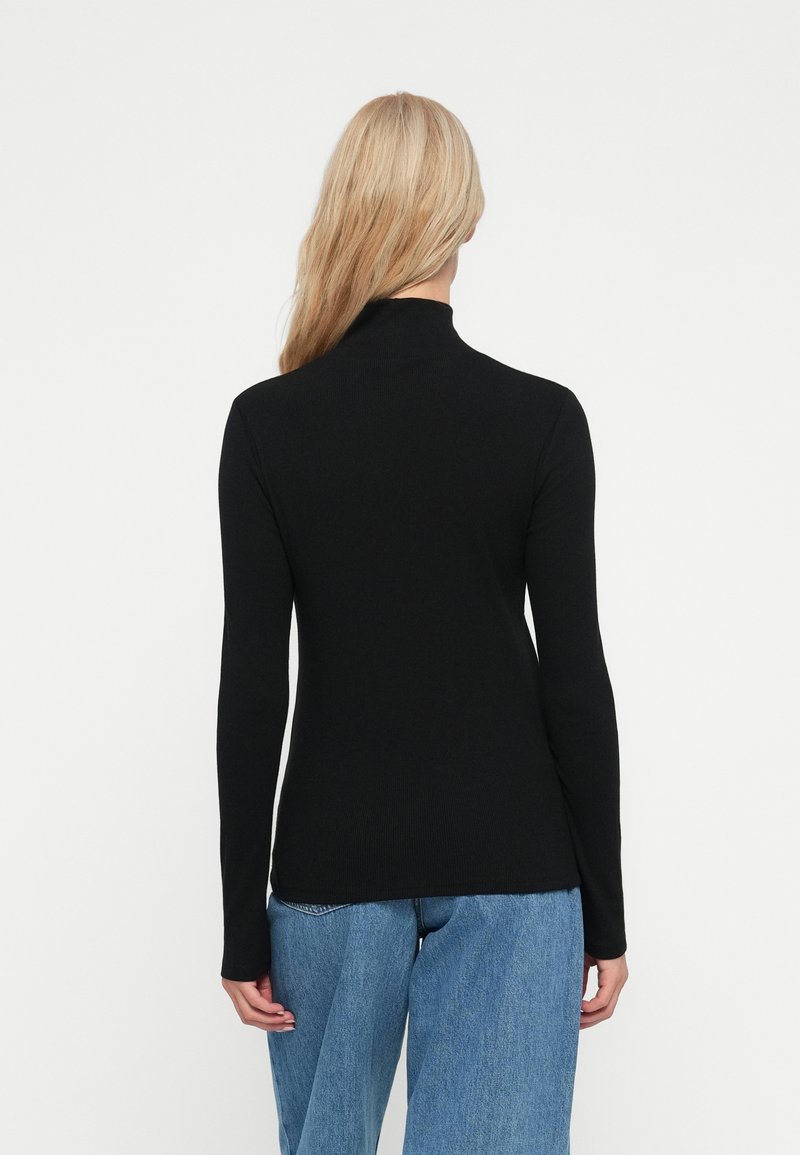 Maglione nero a collo alto con maniche lunghe, design aderente, texture a coste e colletto alto, abbinato a jeans a gamba larga blu chiaro.