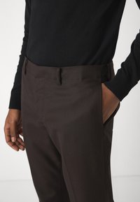 Brune stripete bukser med slim fit, med sidelommer og flat front, kombinert med en svart langermet topp.