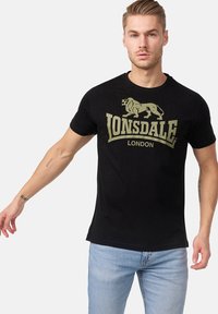 Fekete pamut póló, nagy, világoszöld oroszlán logóval és vastag betűkkel írt "LONSDALE LONDON" felirattal. Rövid ujjú, kerek nyakú kialakítás.