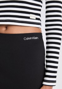 Crna pamučna suknja s bijelim "Calvin Klein" logotipom na struku, uparena s crno-bijelim prugastim kratkim topom.