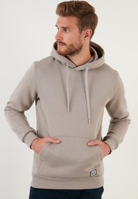 Sudadera gris clara con un bolsillo canguro en la parte frontal, cordón ajustable y puños acanalados. Tejido suave con un corte casual y detalle de etiqueta de marca.