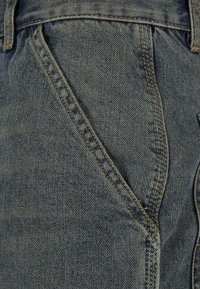 Denim fabric in dark blue with a textured finish. Features visible stitching and a side pocket detail, emphasizing shape and structure.
