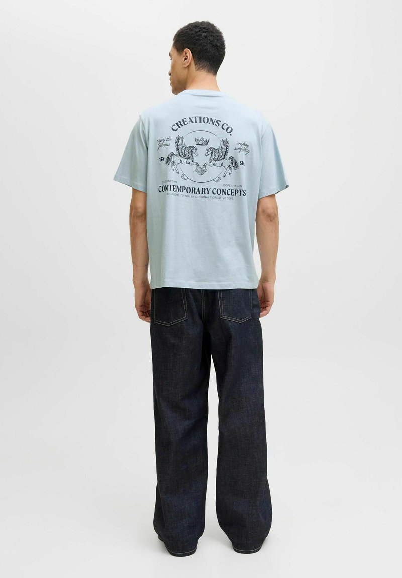 Lyseblå T-shirt med korte ærmer og grafisk print med løver og tekst på ryggen, parret med mørkeblå vide jeans.