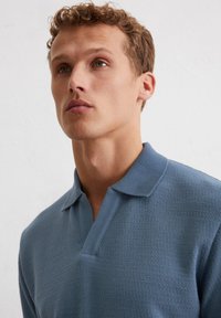 Polo shirt blu textured con colletto a costine, con placca a mezza bottoni. Tessuto morbido che aderisce delicatamente al corpo.