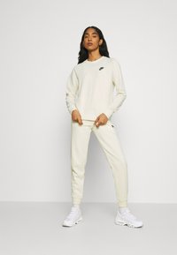 Conjunto de sweatshirt e calças de moleton brancas da Nike com punhos canelados, decote redondo e logotipo no peito e na coxa, combinado com sapatilhas brancas.