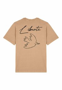 T-shirt en coton beige avec un contour noir d'une colombe et le mot "Liberté" au-dessus, situé à l'arrière. Manches courtes et col rond.