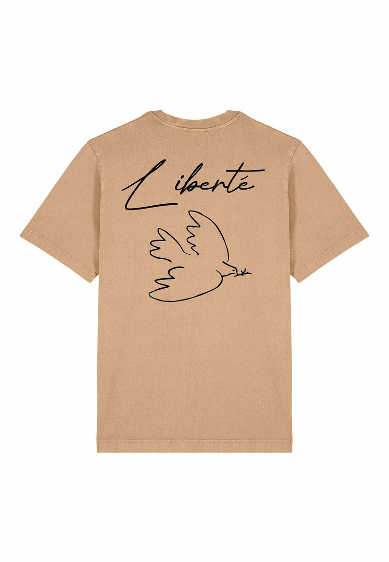T-shirt en coton beige avec un contour noir d'une colombe et le mot "Liberté" au-dessus, situé à l'arrière. Manches courtes et col rond.