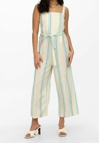 Combinaison rayée en tissu léger, avec un décolleté carré, des jambes larges et une ceinture nouée à la taille. Les couleurs incluent des tons pastel et neutres.