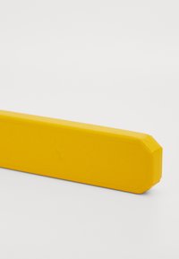 Keltainen suorakaiteen muotoinen palkki, jossa on viistetyt reunat, sileä pinta ja logopainatus. Hiukan pyöristetyt kulmat luovat vankan ja kompaktin ulkonäön.