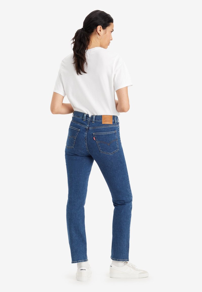 Jeans en denim bleu avec un design ajusté, taille mi-haute et poches arrière. Associés à un t-shirt blanc uni et des baskets blanches.