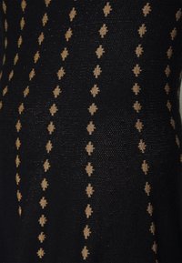 Tissu noir présentant un motif texturé avec des formes de losange dorées disposées en lignes verticales, créant un motif subtil.