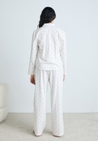 White pajama set with red polka dots, featuring a collared long-sleeve top and loose-fitting pants, made from a soft, lightweight fabric.